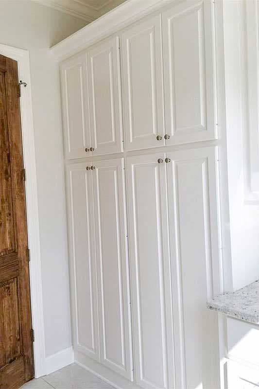 Tall white Shaker-style cabinets with paneled doors and decorative hardware in a room with a wooden door.