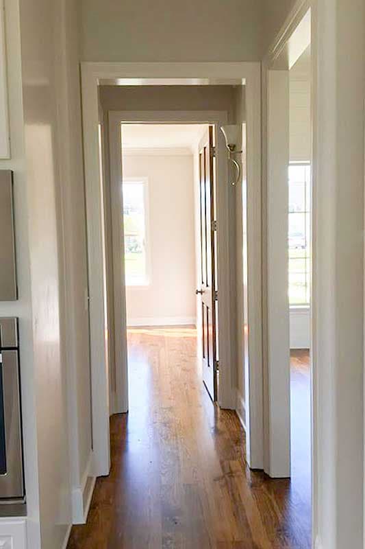 Interior hallway with hardwood floors, leading to rooms with windows and white trim.