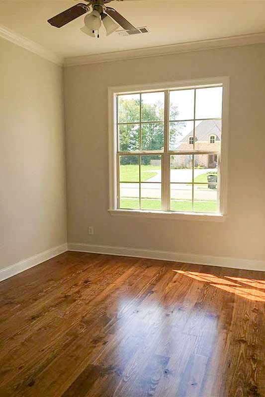 Interior room with wood flooring, crown molding, ceiling fan, and large multi-pane window showing a house exterior.