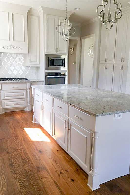 Kitchen featuring white cabinetry, granite island, stainless steel appliances, tiled backsplash, and hardwood floors.