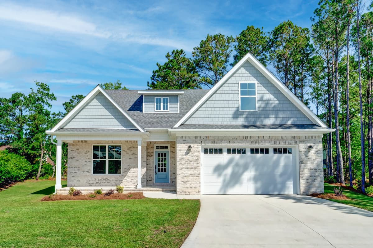 House plan exterior. One-story Ranch style home with gabled roof, brick facade, and front-entry garage. Porch supported by columns.