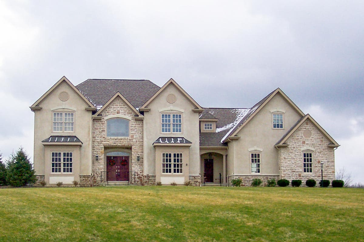 House plan exterior. Two-story home with a stone facade, multiple gables, and a prominent entryway. Features include dormers and arched windows.