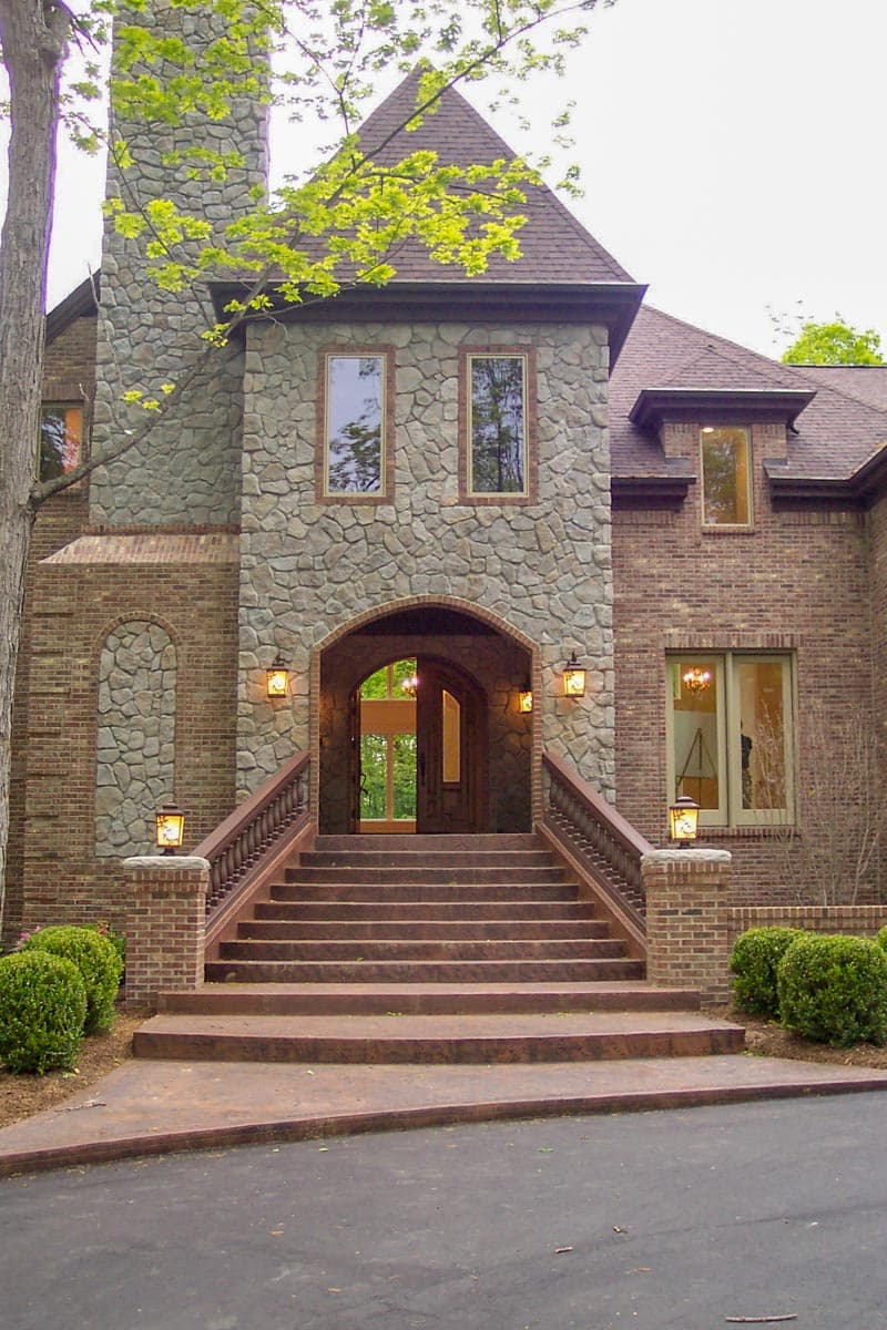 House plan exterior with stone and brick facade, grand staircase, arched entryway, and prominent stone chimney.