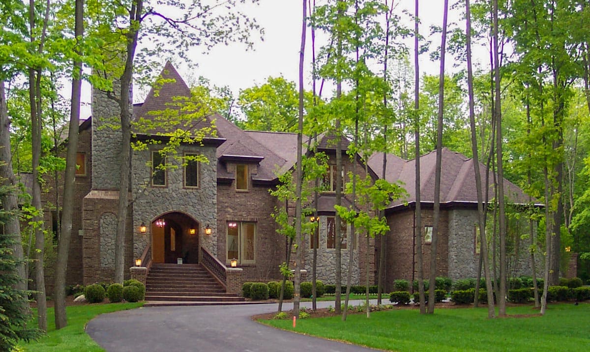House plan exterior. Two-story home with stone and brick facade. Features include a turret, arched entryway, and multiple gables.