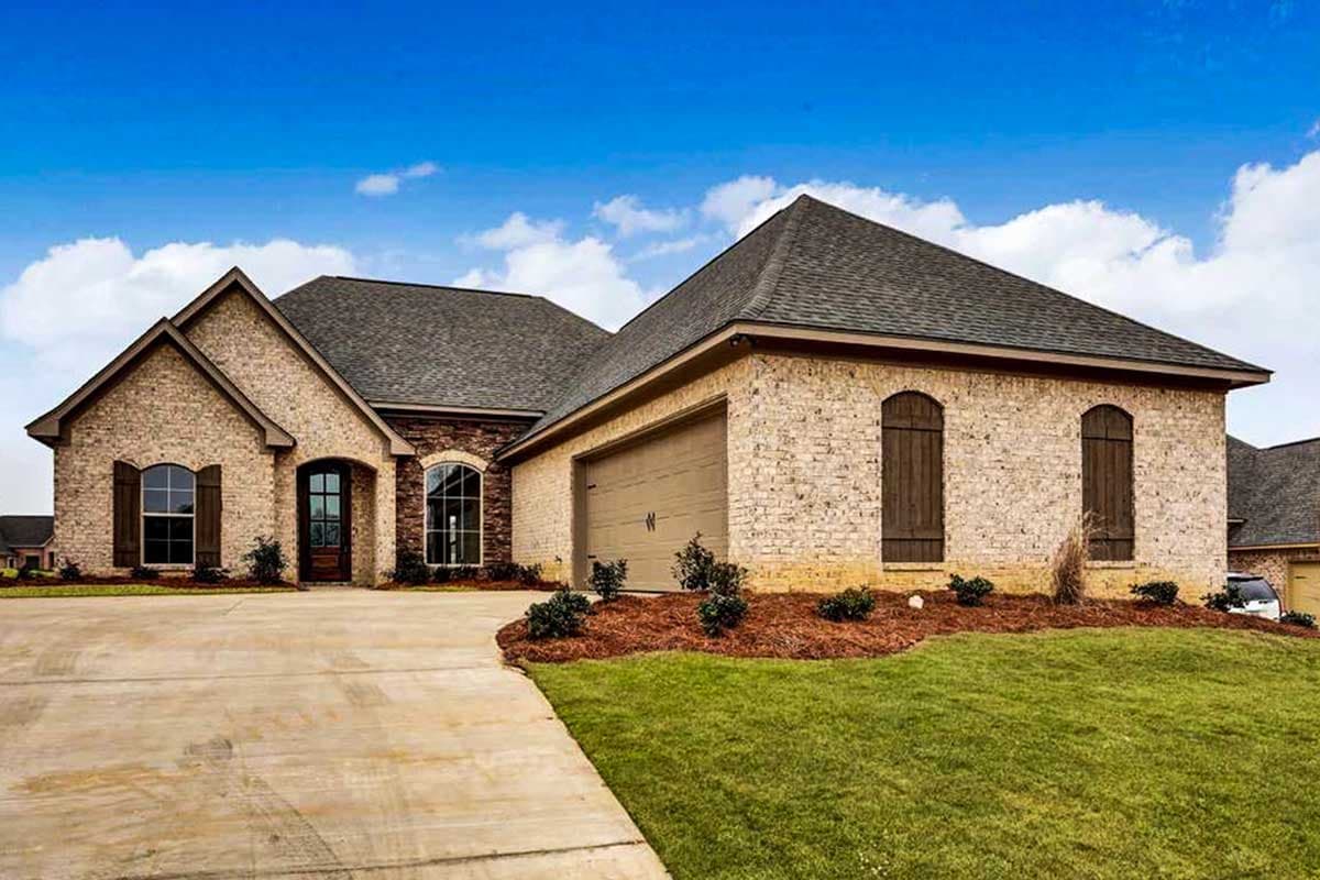House plan exterior with brick facade, gable roof, and attached garage. Includes arched windows with wooden shutters and a concrete driveway.