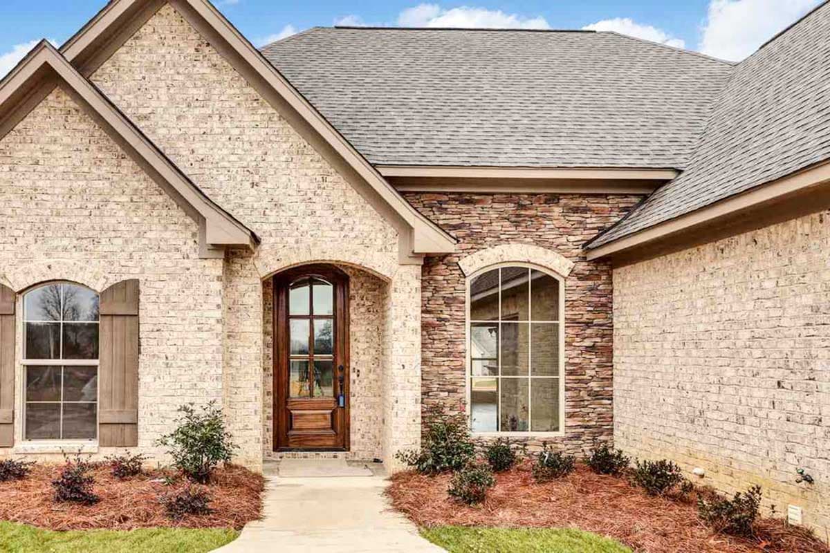 House plan exterior with light brick, stone accents, arched entry door, and arched window with shutters.