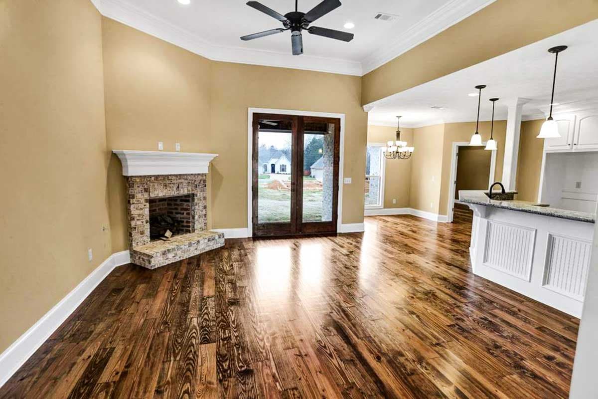 Interior view of a house plan showing a great room with a brick fireplace, vaulted ceiling, fan, and view of kitchen with island.