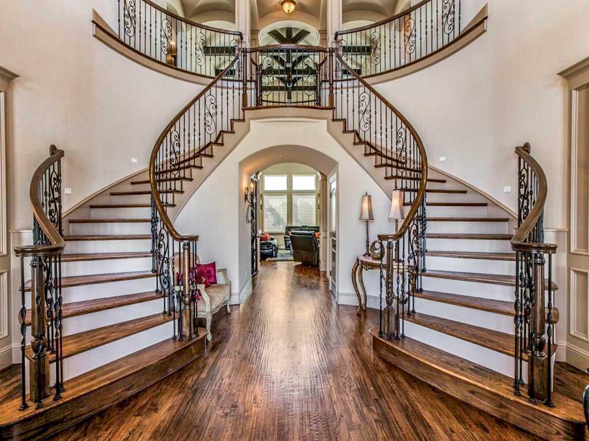 Grand foyer with a sweeping dual staircase, ornate iron railings, arched entryway, and hardwood floors.