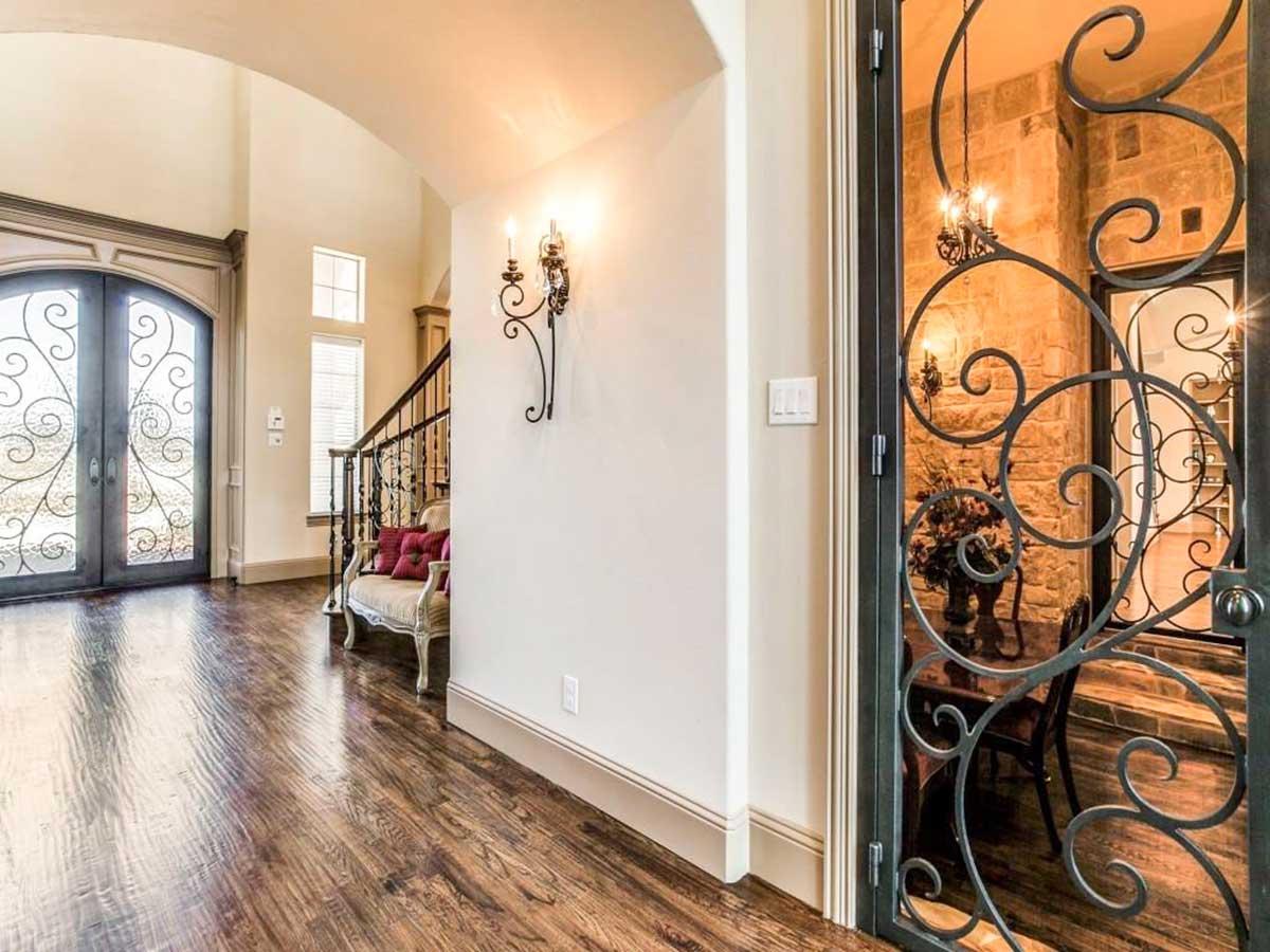 Interior view of a house foyer with double doors, ornate wrought iron gate, staircase, and sconce lighting.