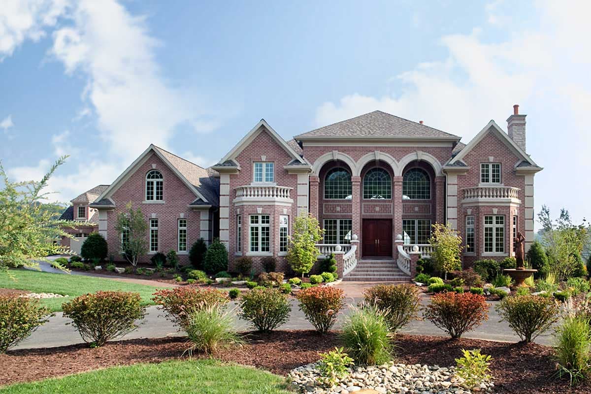 House plan exterior. Two-story brick home with arched windows and entryway, balustrade balconies, multiple gables, and a prominent roofline.
