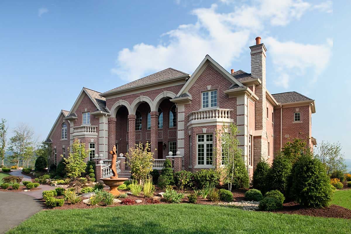 House plan exterior of a large, two-story brick home with arched windows, decorative balustrades, and a prominent chimney.