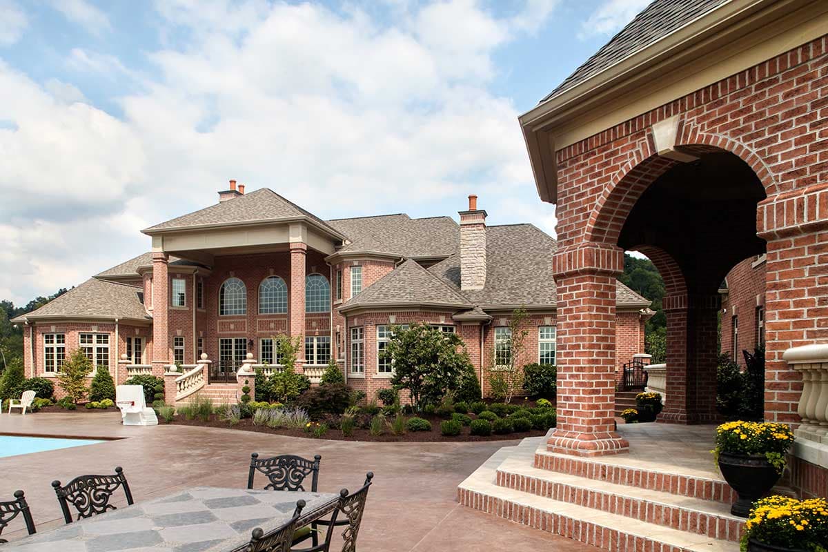 House plan exterior of a large brick mansion with a grand portico, arched windows, multiple gables, and a tiled roof.