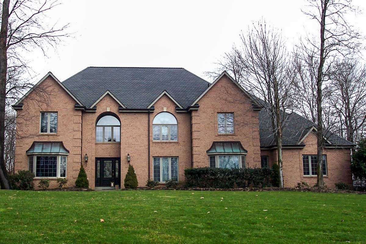 House plan exterior. Two-story brick home with gabled roof, arched and rectangular windows, and two bay windows. Front entry with arched transom.
