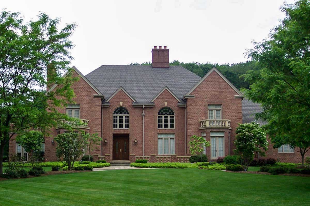 House plan exterior of a two-story brick home with arched upper windows, two balconies, and a prominent chimney.