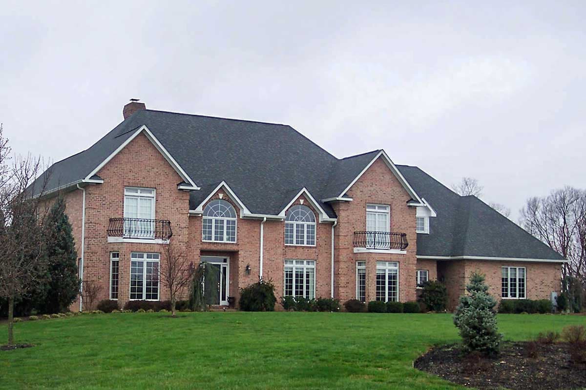 Two-story brick house plan exterior with arched dormers, balconies, and a prominent central gable.