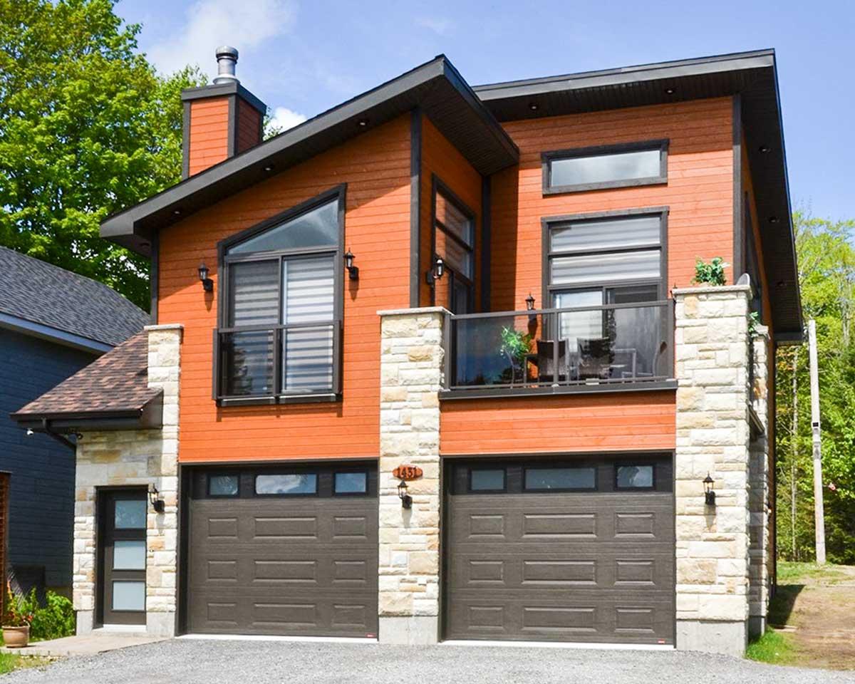 Modern house plan exterior with orange siding, stone accents, dual garage doors, balcony, and unique angled window.