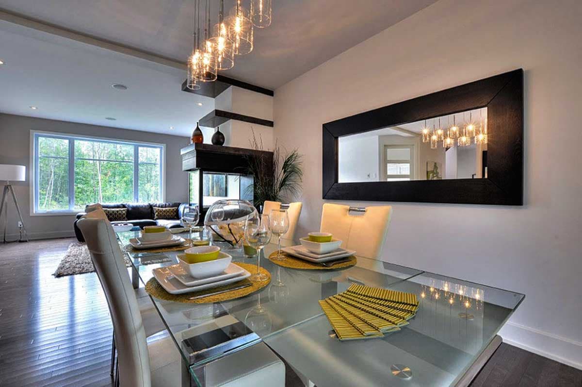 Dining room with glass table, leather chairs, large window, fireplace, and modern chandelier.