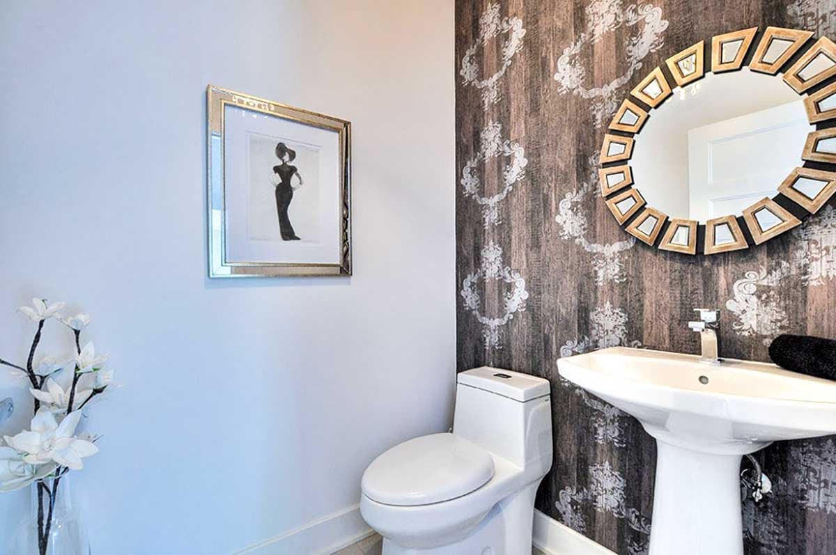 Powder room with pedestal sink, modern toilet, patterned wallpaper, and framed artwork.