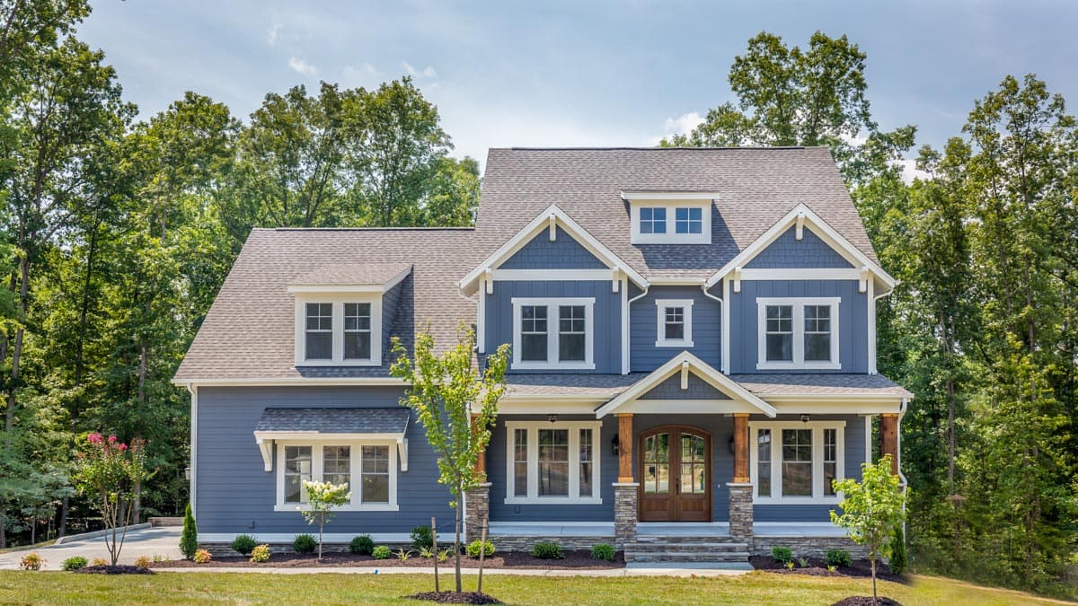 Craftsman-style house plan exterior with blue siding, prominent gables, dormers, and a covered entry with stone accents.