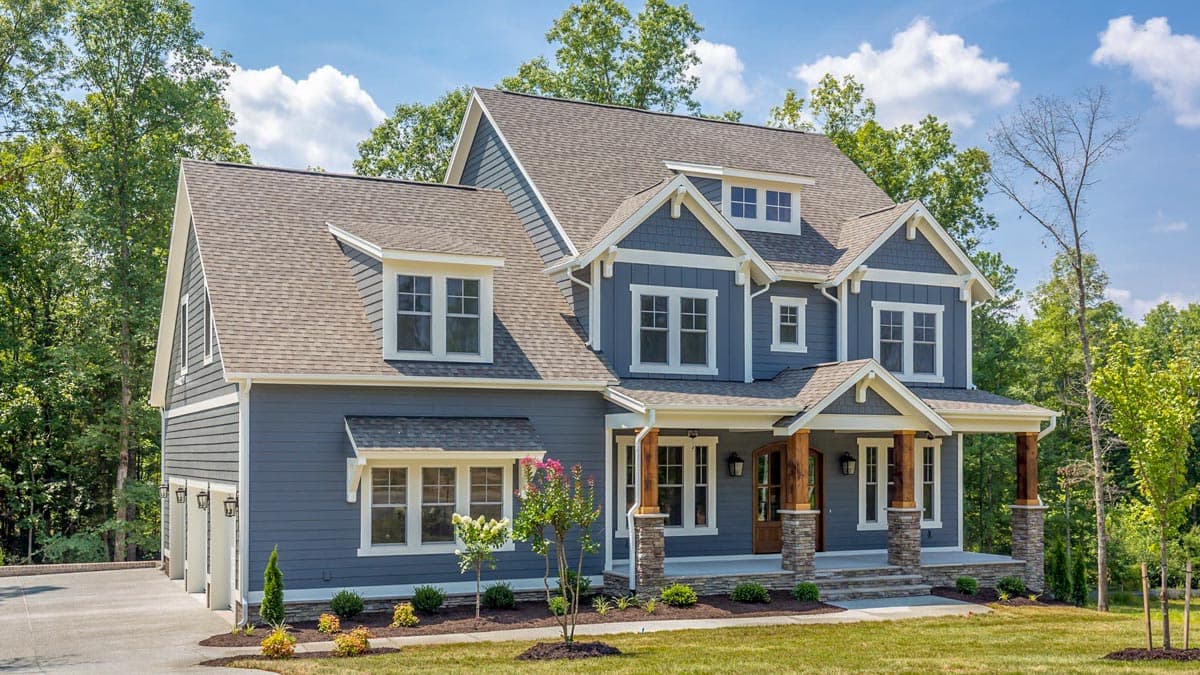 House plan exterior. Two-story Craftsman home with a front porch, gables, and multiple dormers. Includes a three-car garage and a stone-clad porch.