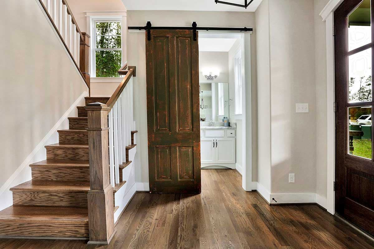 Interior view of staircase and hallway with sliding barn door leading to bathroom vanity with white cabinets.