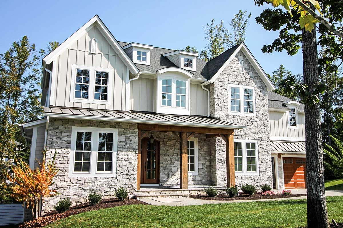 House plan exterior: Two-story home with stone and board-and-batten siding, prominent gables, dormers, and a covered timber-frame entry porch.