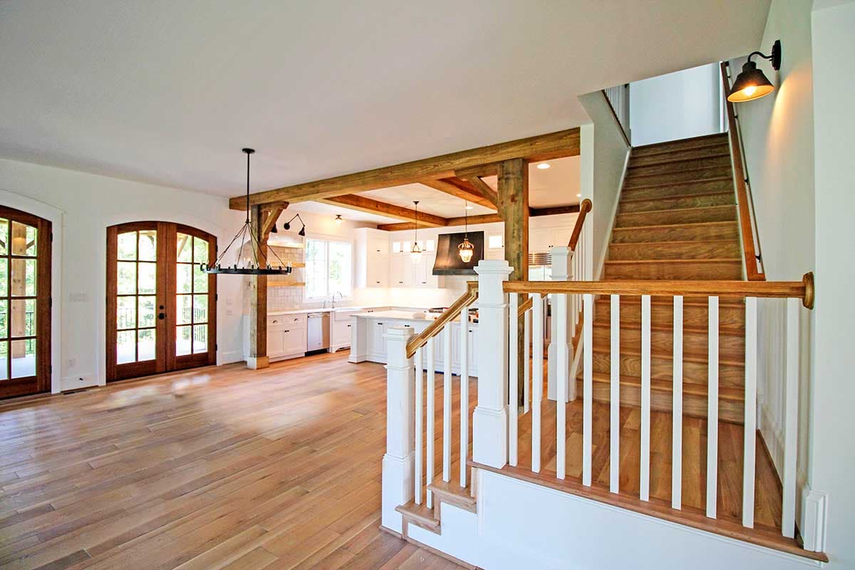Open-concept living area with wood beams, white kitchen cabinets, farmhouse sink, and wood floors.