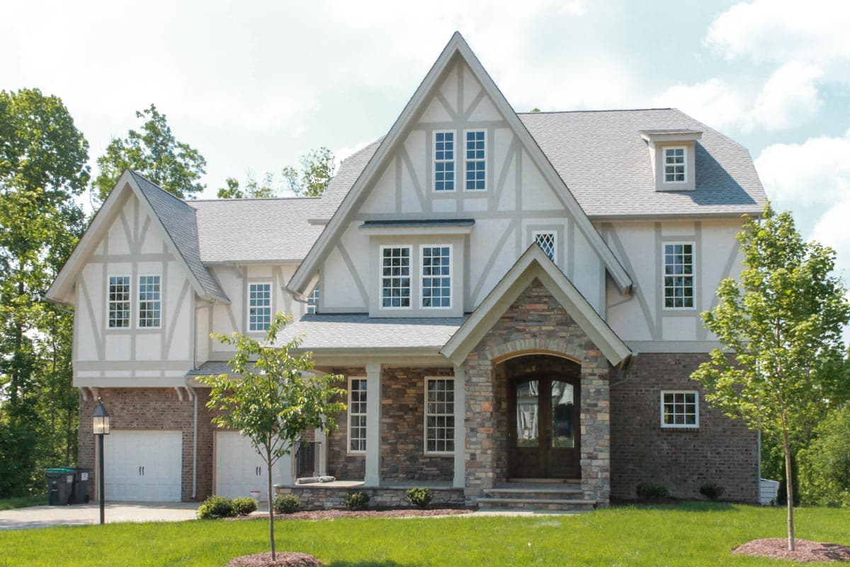 House plan exterior of a two-story Tudor-style home with stone accents, gables, dormers, and a covered porch.