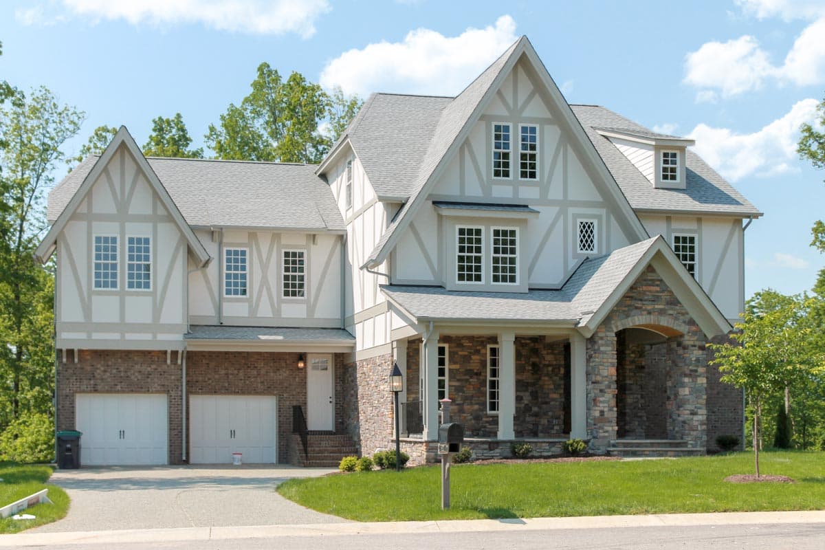 Tudor-style house plan exterior with brick base, multiple gables, dormers, and stone-accented covered entry.