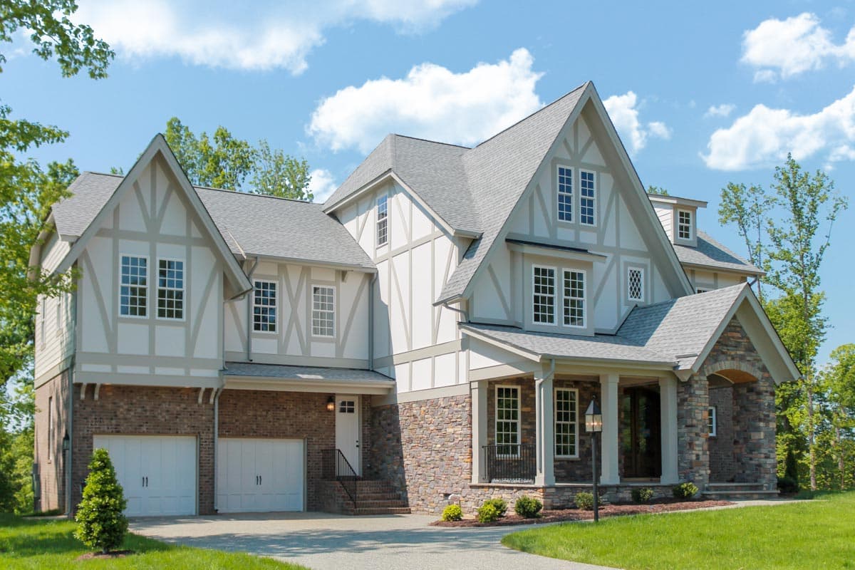 House plan exterior. Two-story Tudor style home with gabled rooflines, stone and stucco facade, and covered front porch.