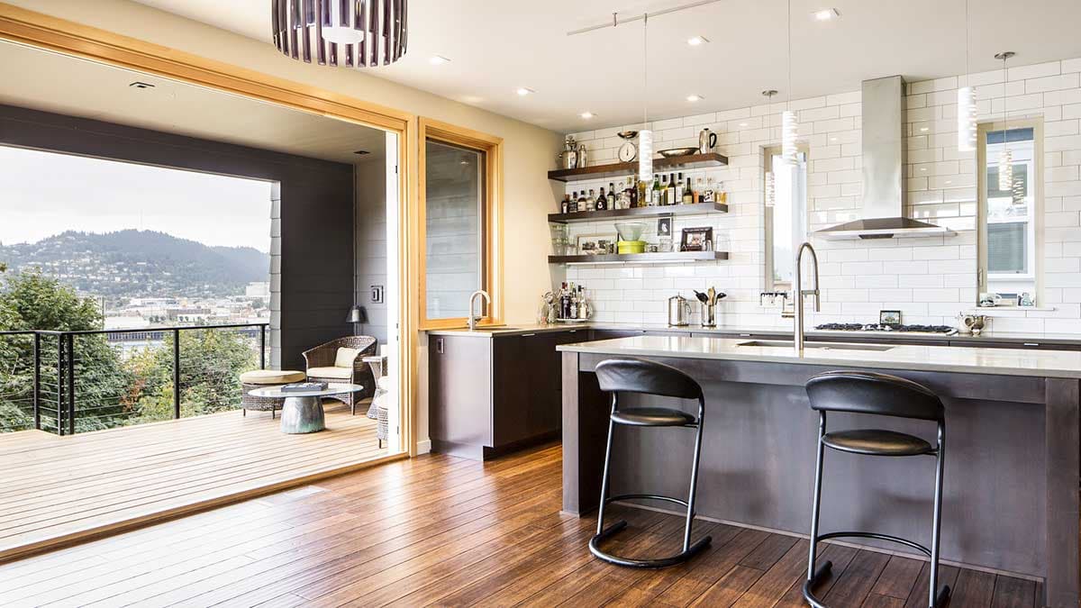 Modern kitchen with island, stainless steel appliances, subway tile backsplash, and access to a wood deck with an expansive view.