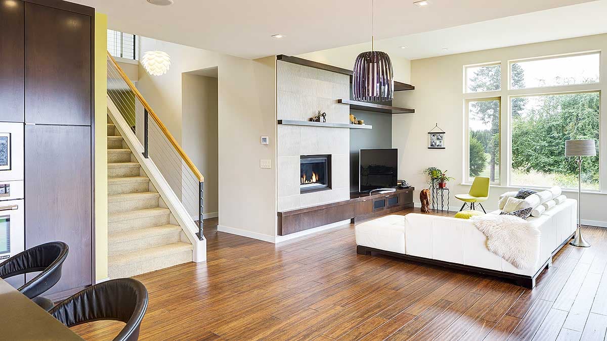 Interior view of modern living room with fireplace, entertainment unit, stairs, and large windows.