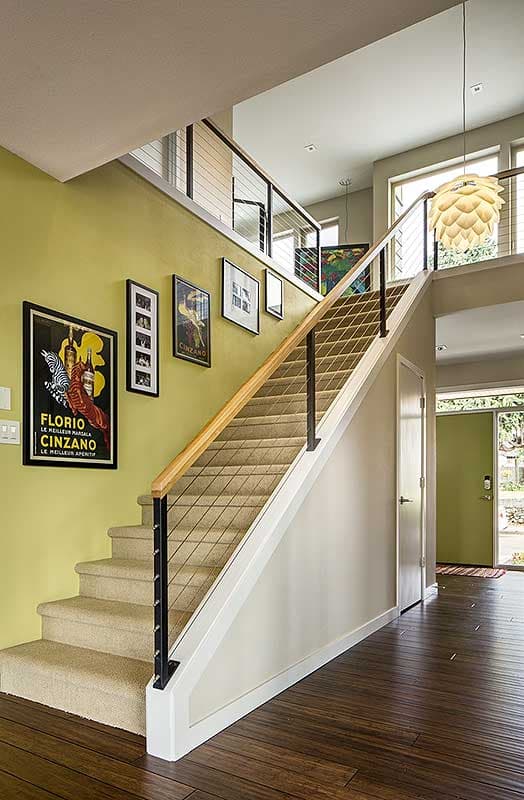 Modern staircase with cable railing, wood handrail, and art on lime green wall. Open landing above.