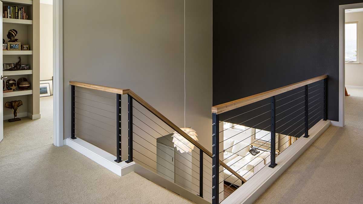 Interior staircase landing with cable railing, wood handrail, and built-in bookshelves.