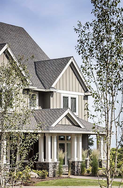 House plan exterior: Two-story home with gables, dormers, stone base, and a covered porch supported by columns.