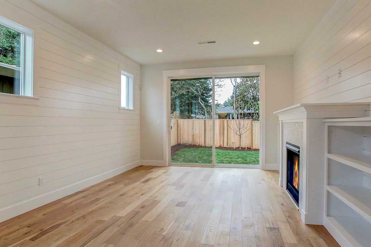 Interior view showing a living room with shiplap walls, fireplace, built-in shelving, and sliding glass doors to the backyard.
