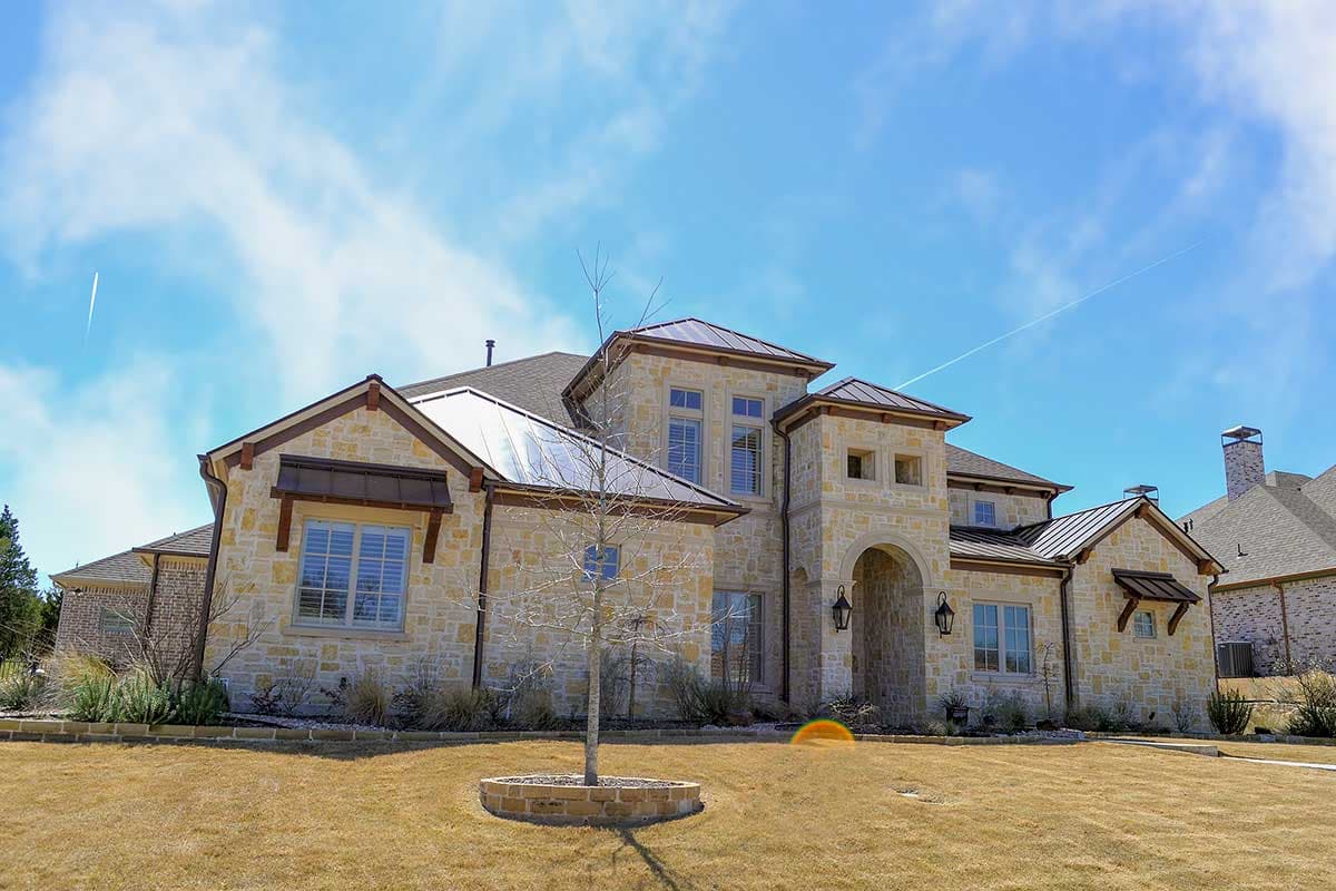 House plan exterior with stone facade, arched entryway, multiple gables, and metal roof.