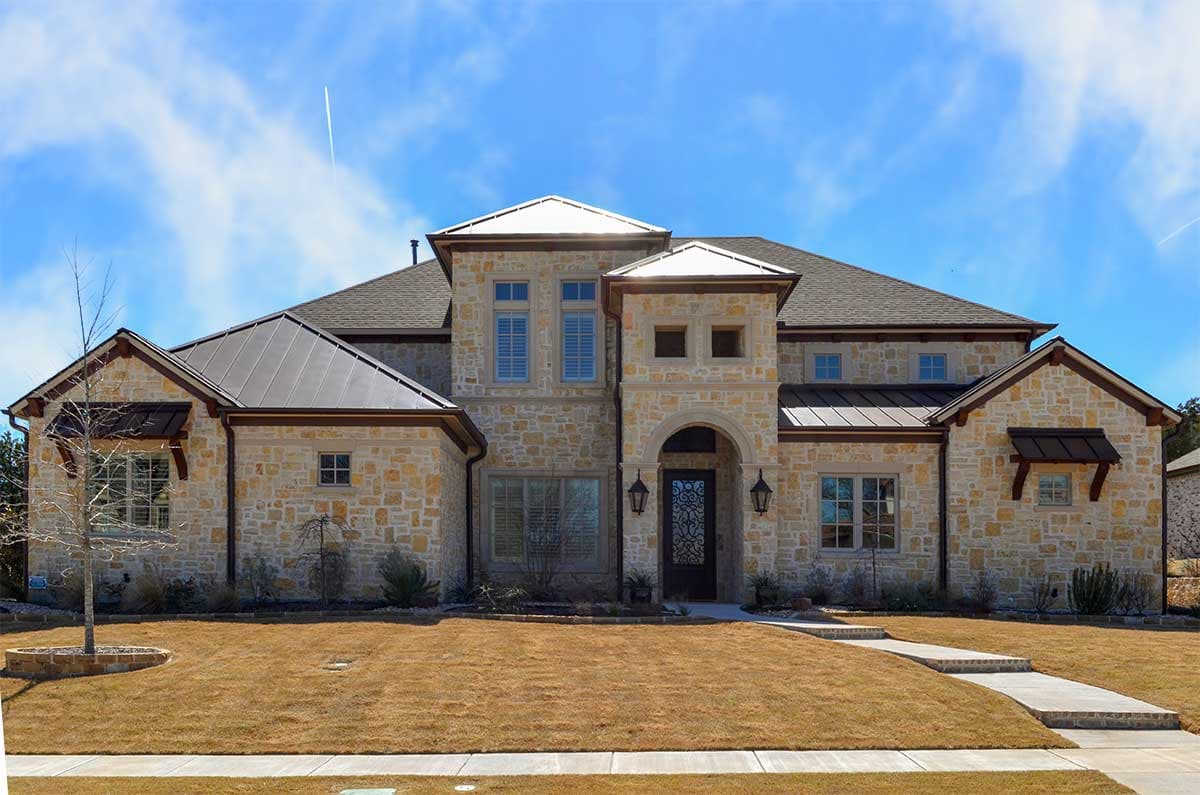 House plan exterior. Stone facade, two stories, arched entryway, metal rooflines, and dormers.