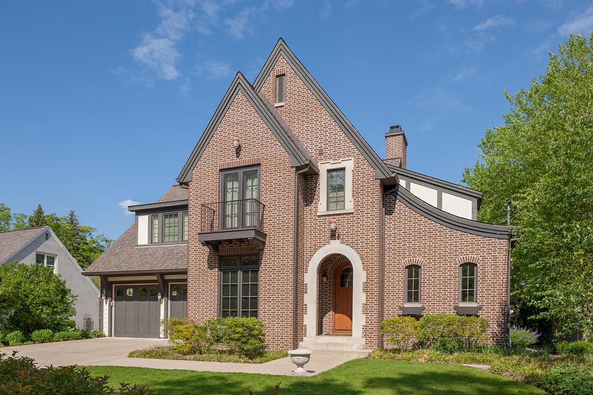House plan exterior with brick facade, two stories, prominent gables, Juliet balcony, arched entry, and attached garage with gabled roof.