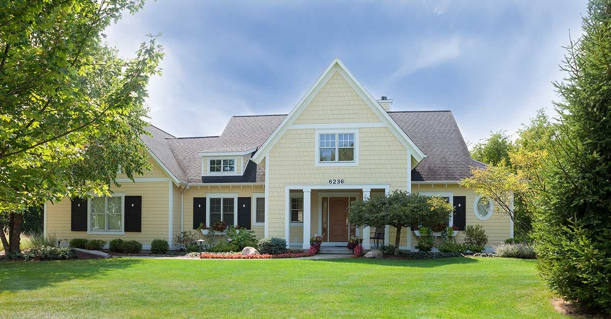 House plan exterior. Two-story Craftsman home with a gabled roof, dormers, and a covered front porch. Features yellow siding and black shutters.