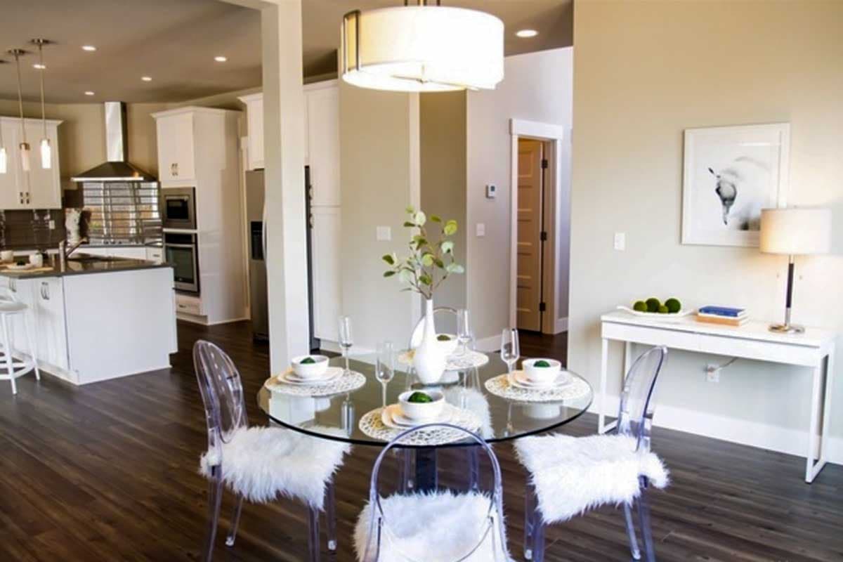 Interior view showing a dining area with a glass-top table and chairs adjacent to a modern kitchen with white cabinetry.