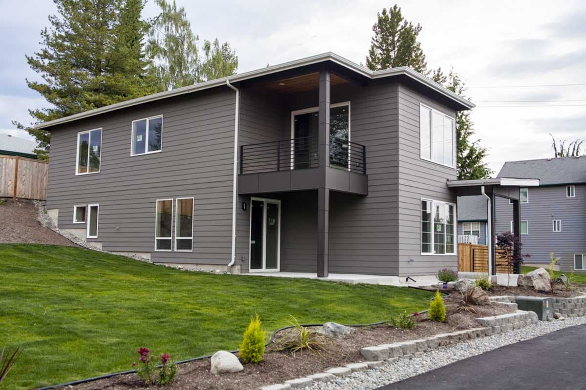 Modern two-story house plan exterior with horizontal siding, cantilevered second-story balcony, and multiple large windows.