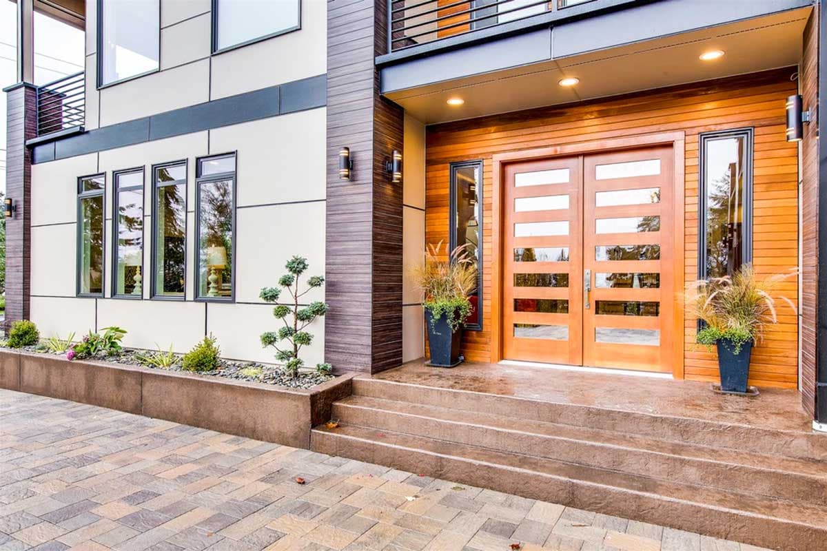 Modern house exterior plan featuring double wooden doors with glass panes, a second-story balcony, and contrasting facade materials.