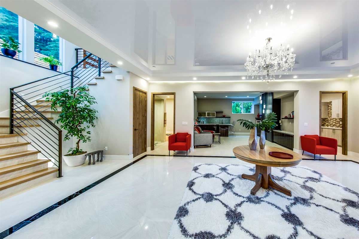 Interior view of a modern house entry with a floating staircase, open layout to kitchen and dining, and a crystal chandelier.