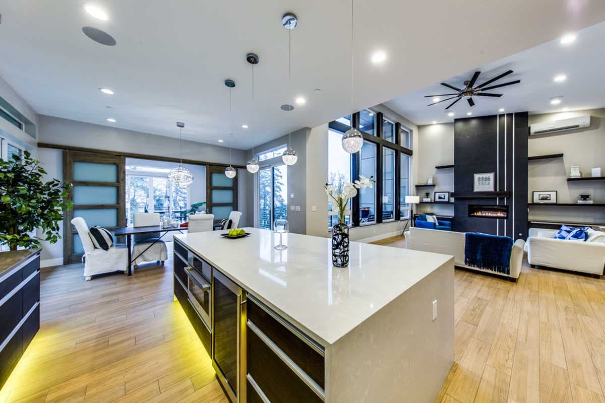 Modern open-concept living area with kitchen island, dining area, fireplace, and large windows.
