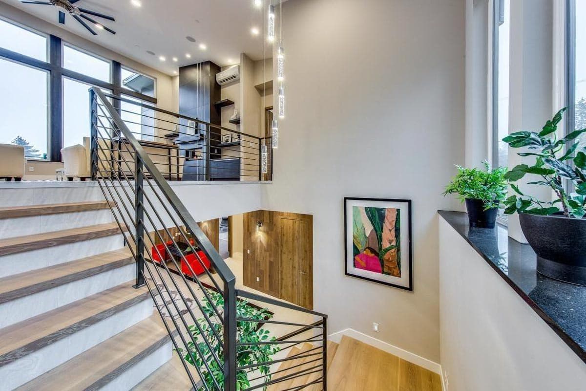 Modern house interior with open-concept living, floating stairs, metal railings, and large windows.