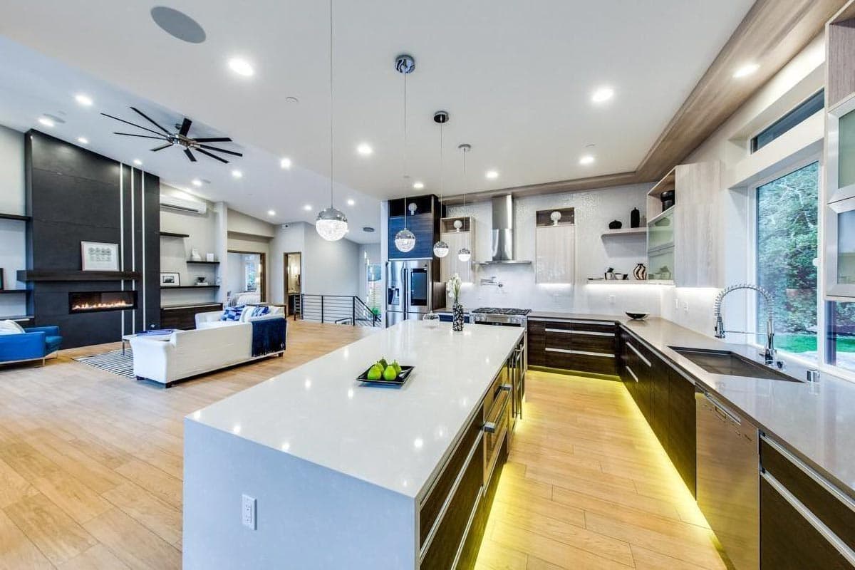 Open concept living space with a modern kitchen featuring a large island and stainless steel appliances, adjacent to a living area with a fireplace.