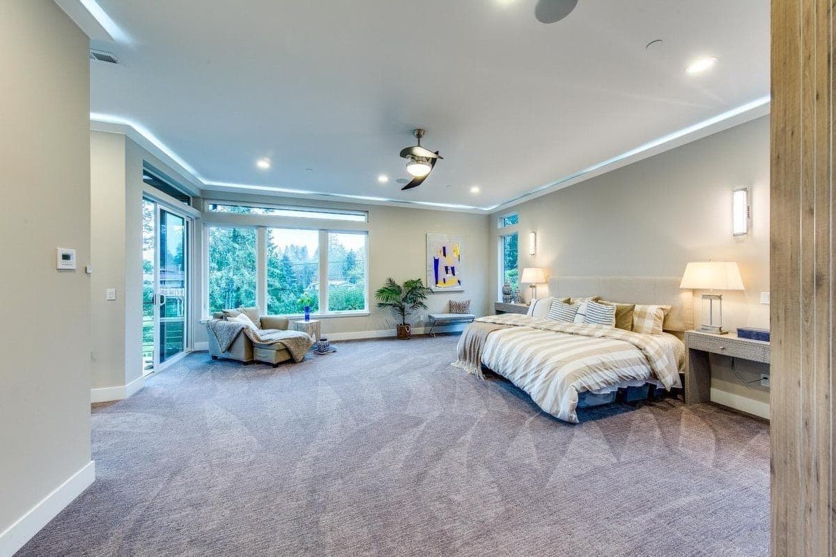 Spacious bedroom with large windows, king-size bed, seating area, and vaulted ceiling with recessed lighting.
