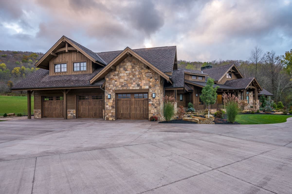 Craftsman style house plan exterior with three-car garage, stone accents, gable rooflines, and exposed rafter tails.