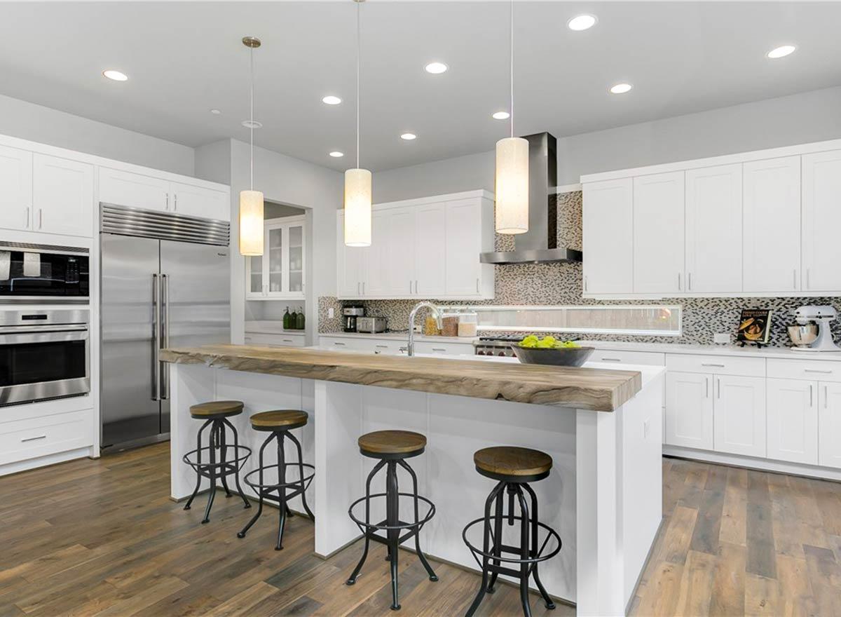 Modern kitchen with white cabinetry, stainless steel appliances, island with live-edge wood countertop, and pendant lighting.